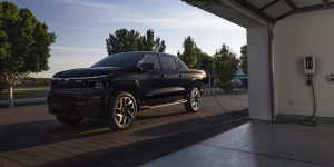 A 2025 Chevy Silverado EV parked outside of a home while being charged by a home charging station. 