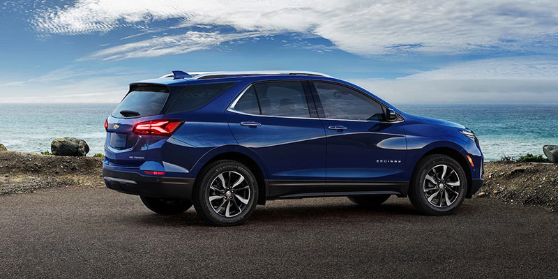 Rear passenger side view of a blue 2022 used Chevy Equinox parked by a lake with blue skies overhead