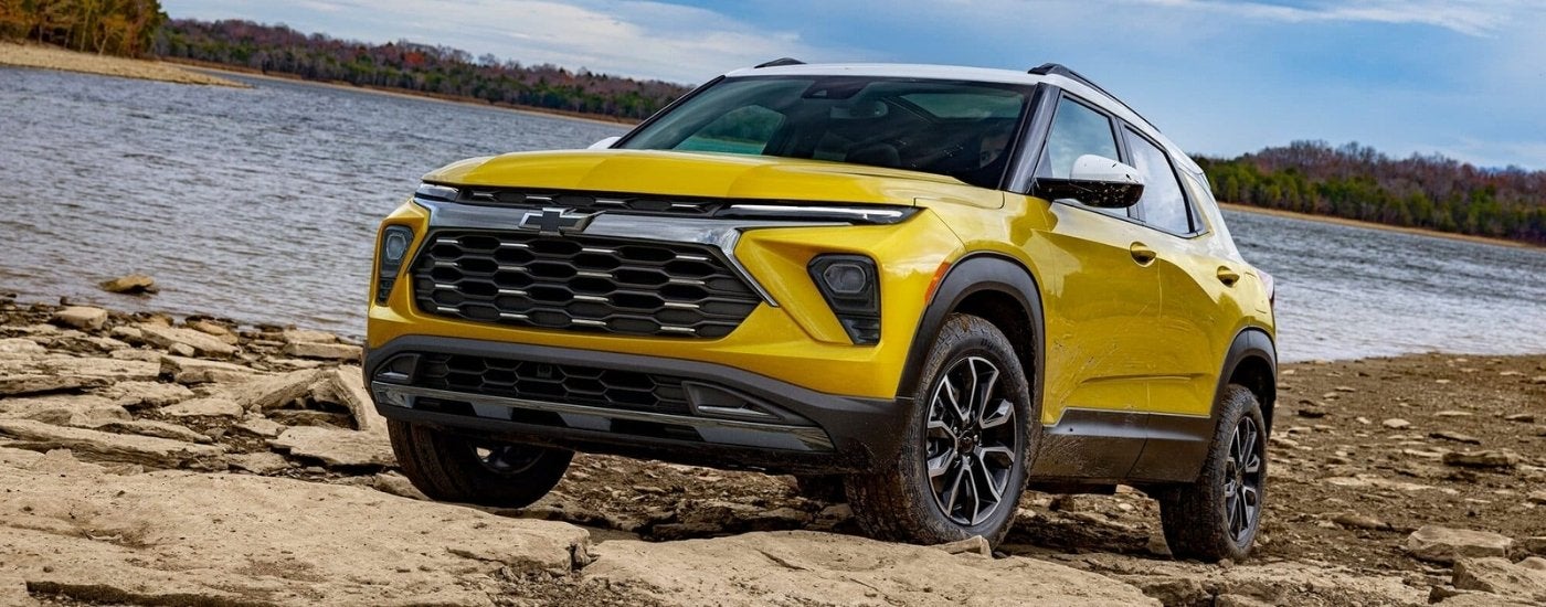 A yellow 2025 Chevy Trailblazer parked on a rocky beach.
