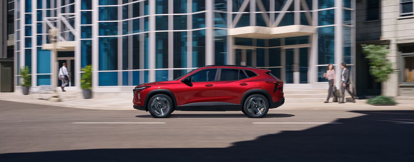 Side of a red 2026 Chevy Trax driving down a city street.