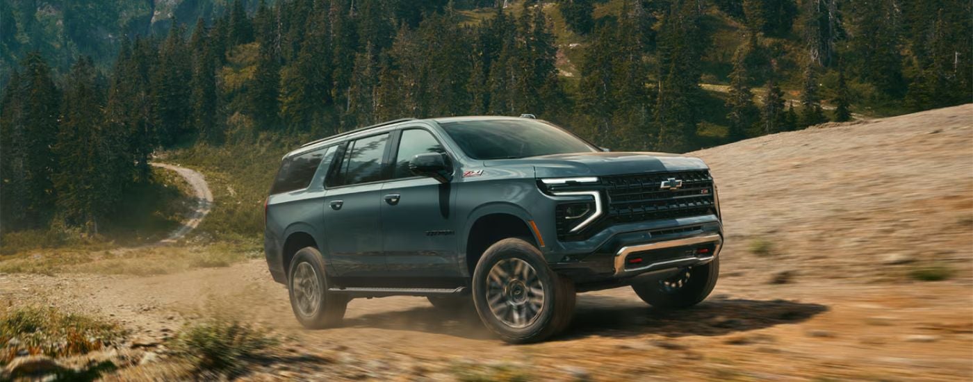 Green 2026 Chevy Suburban drivin off-road on a mountain.