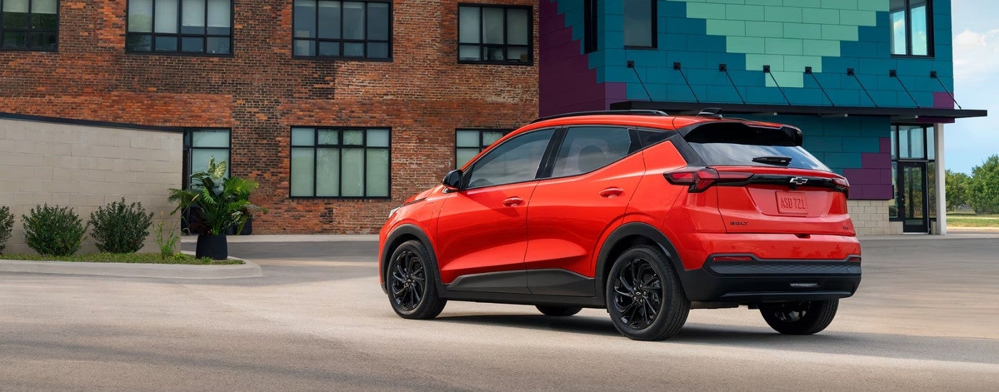 Rear of an orange 2026 Chevy Bolt parked in front of a brick building