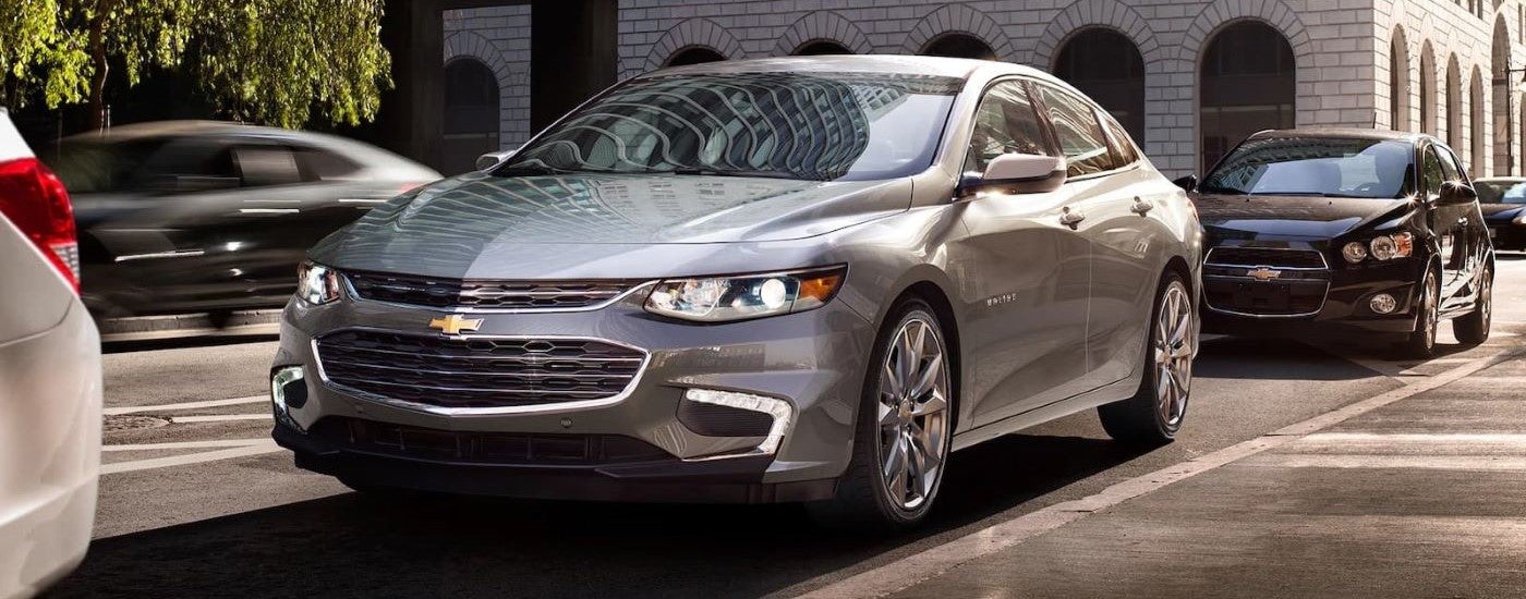 A silver 2018 Chevrolet Malibu driving in a city.